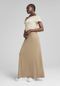 Beige maxi skirt med en glat tekstur, parret med en lys gul t-shirt med et hvidt logo, og accessoriseret med et leopardmønstret tørklæde.