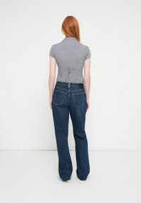 Kortærmet, ternet grå bluse med krave og snøre detalje på ryggen, kombineret med blå, vidde jeans i denim.