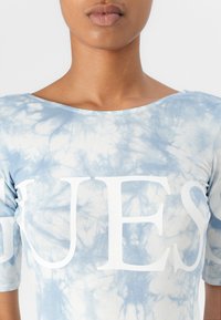 T-shirt blu tie-dye con maniche corte e scollatura rotonda. Presenta grande testo bianco sul petto, con una texture morbida e liscia.