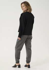 Top negru cu mâneci lungi și umeri drapate, asortat cu pantaloni gri cu talie elastică și mules negre cu toc bloc și degetele expuse.