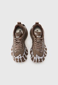 Pantofi sport maro cu un material superior din plasă texturată, accente grafice albe contrastante și un design de talpă masivă. Șireturile și logo-ul sunt vizibile.