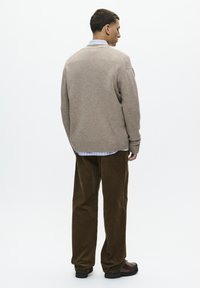 Beige strikket sweater med en afslappet pasform, ribbede manchetter og kant. Parret med brune kordfløjlsbukser og mørke sko. Bagudsigten.