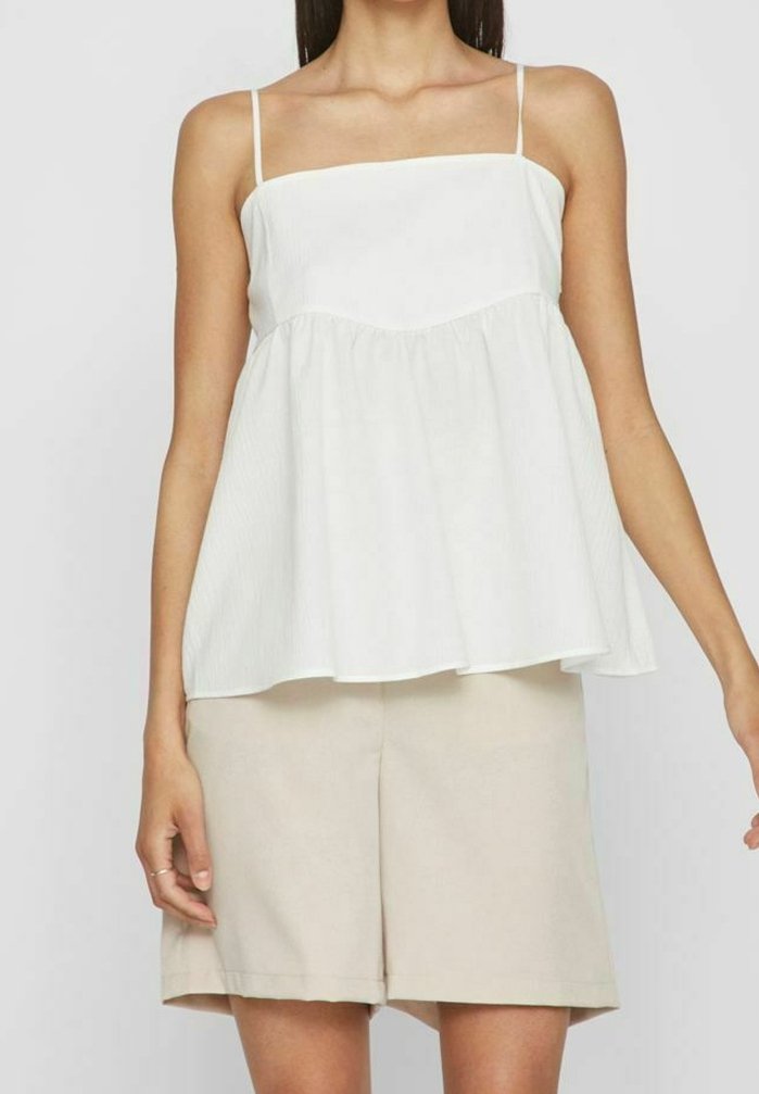 Vit, ärmlös topp med fyrkantig utskärning och flödande, rynkad nederkant. Tillverkad av ett lätt tyg med subtil textur. Kombineras med beiga shorts.
