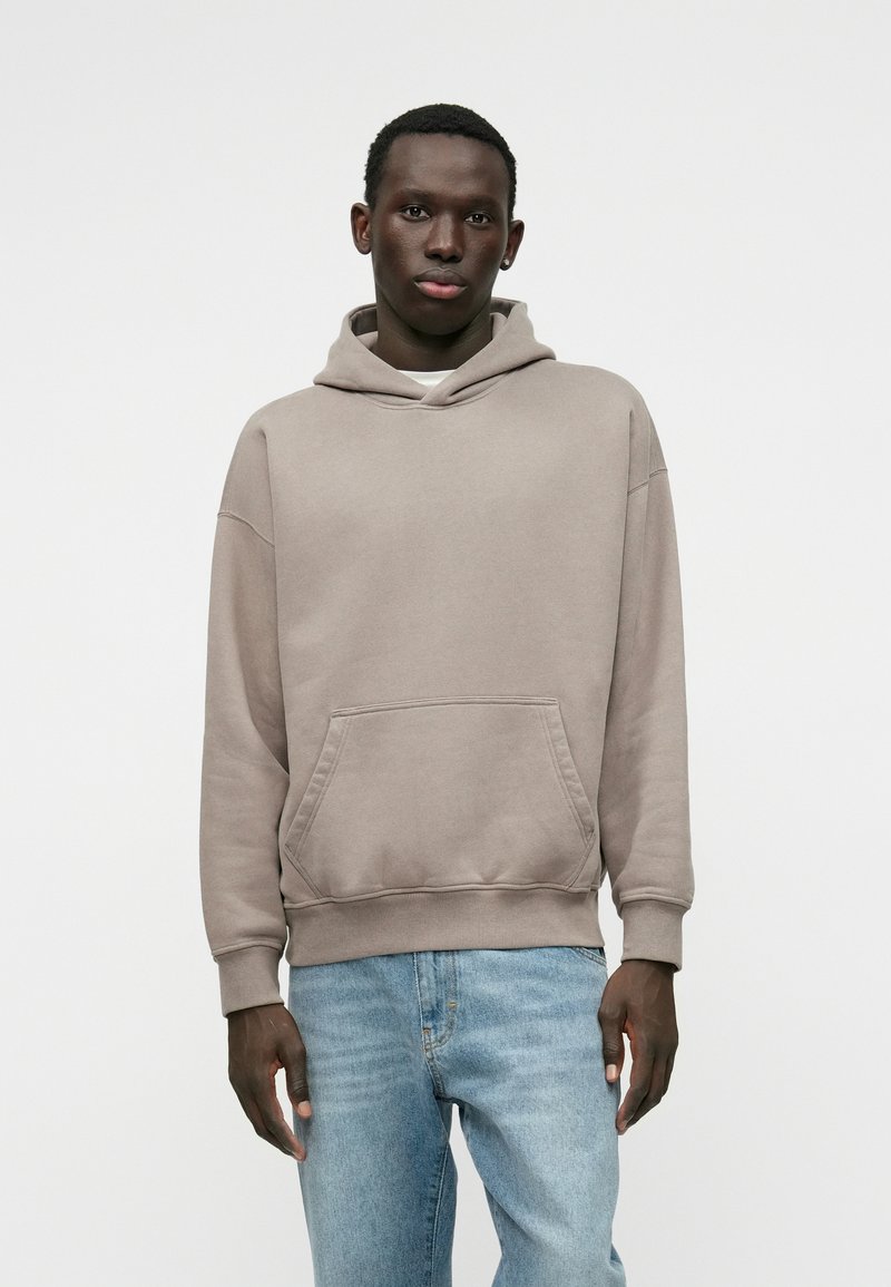 Καφετί βαμβακερό φούτερ με κουκούλα, διαθέτει μπροστινή τσέπη και ραμμένο στρίφωμα, συνδυασμένο με ανοιχτό μπλε τζιν παντελόνι. Λείος υφασμάτινος χαρακτήρας, χαλαρή εφαρμογή.