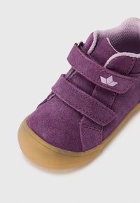 Sapato de camurça roxo com duas correias de Velcro ajustáveis, sola de borracha e forro suave no interior. Logo da marca em roxo claro na lateral.