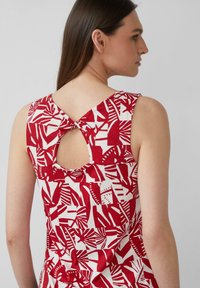 Mouwloze top in rood en wit met een patroon, voorzien van een sleutelgatdetail aan de achterkant. Gemaakt van een lichte stof met een geometrische print.