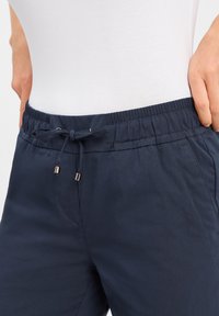 Marineblauwe, lichte broek met een elastische tailleband en verstelbaar trekkoord. Voorzien van zilverkleurige hardware en zijzakken.