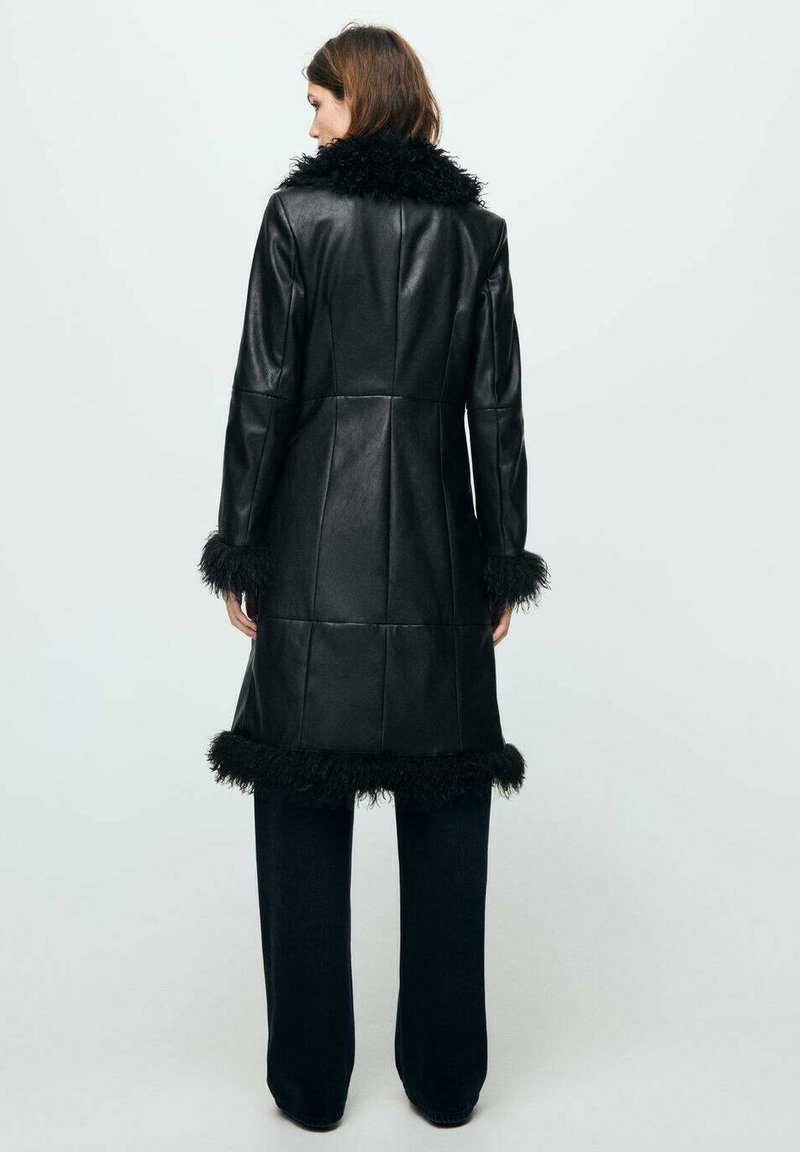 Palton din piele neagră cu guler și mansete din blană sintetică, având un design ajustat și un finisaj texturat. Purtați peste pantaloni largi de culoare închisă.