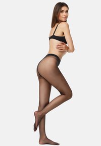 Gennemsigtige sorte strømpebukser med en glat finish, høj talje og sømløs tå-design, båret sammen med en sort bh mod en ensfarvet baggrund.
