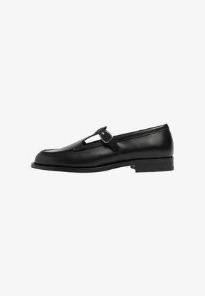 Schwarze Lederloafers mit T-Riegel-Design und Schnallendetails, flache Sohle, glatte Textur und genähte Akzente entlang der Kanten.