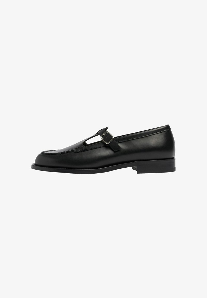 Schwarze Lederloafers mit T-Riegel-Design und Schnallendetails, flache Sohle, glatte Textur und genähte Akzente entlang der Kanten.