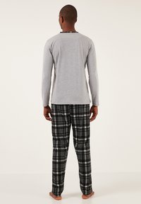 Tricou bărbătesc gri cu mânecă lungă, cu guler cu carouri negre, asociat cu pantaloni de pijama cu carouri negre și gri. Material moale, croială lejeră.