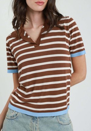 Donna che indossa un top a maniche corte a righe orizzontali marroni e bianche con bordatura blu abbinato a jeans denim azzurri chiari.