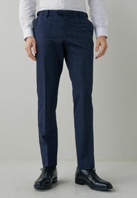 Kalhoty s námořnickým vzorem, slim fit, s poutky na opasek, doplněné o černé šněrovací formální boty na světle šedém pozadí.