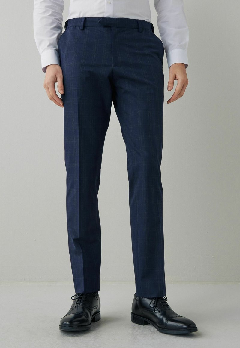 Kalhoty s námořnickým vzorem, slim fit, s poutky na opasek, doplněné o černé šněrovací formální boty na světle šedém pozadí.