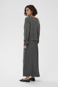 Pull en tricot gris à coupe ample, associé à une longue jupe en satin gris et des ballerines noires, vu de derrière. Texture douce et design décontracté.