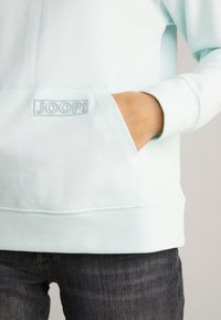 Light blue sweatshirt with a hood, front pocket, and embroidered "JOOP!" logo. Fabric is smooth, medium weight, with ribbed cuffs.