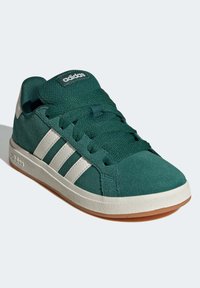 Gröna mockasneakers med vita ränder, rund tå, strukturerad ovandel, vadderad krage och gummisula. Logotyp synlig på tungan och sidan.