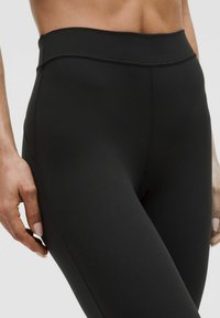 Černé legíny s vysokým pasem vyrobené z hladkého, elastického materiálu. Mají bezešvý design, který se přizpůsobí jako druhá kůže a nemají viditelné švy.