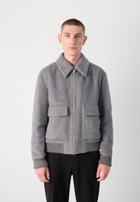 Gray herringbone-pattern jacket with a zip front, wide collar, two front pockets, and ribbed cuffs. Soft, textured fabric.