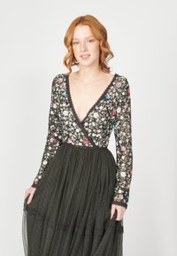 Vestido de manga larga con escote en V profundo, cuerpo de lentejuelas florales y falda oscura de color verde, con capas, patrones de puntos y borde de encaje.