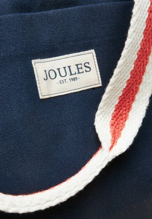 Tissu bleu marine avec une étiquette blanche portant l'inscription "JOULES - EST. 1989" et une sangle tricotée ou tissée rayée blanche et rouge.