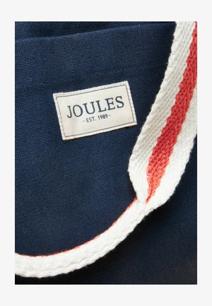 Tissu bleu marine avec une étiquette blanche portant l'inscription "JOULES - EST. 1989" et une sangle tricotée ou tissée rayée blanche et rouge.