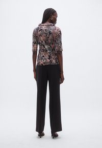 Floral-patterned top in black, featuring short sleeves and a cowl neckline, paired with high-waisted black pants and heels.