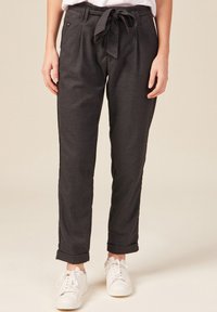 Grå, skräddarsydda byxor med bälte i midjan, sidfickor och uppvikt fåll. Tillverkade av ett slätt tyg, kombinerade med vita sneakers.