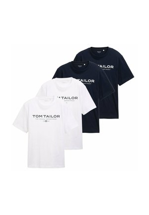 Joven con una camiseta azul marino de Tom Tailor y pantalones beige con las manos en los bolsillos, frente a un fondo claro y liso.