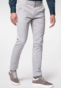 Světle šedé kalhoty se slim fit, vyrobené z měkké tkaniny, s bočními kapsami, nošené s šedými a bílými sportovními botami.