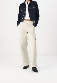 Džínová bunda má světle modrou barvu, klasický střih a kovové knoflíky. Béžové cargo kalhoty s kapsami, střih na míru a šňůrkami na kotnících. Černé boty na podpatku.