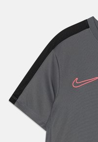 Camiseta atlética gris de manga corta, con acentos de malla negra en los hombros y un logo de Nike en color rosa neón en el pecho.