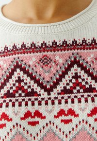 Gebreide trui met een crèmekleurige basis en patronen in rood, roze en grijs. Ribgebreide hals, geometrische ontwerpen en lipmotieven zijn inbegrepen.