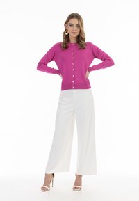 Cardigan a maglia fucsia con scollo rotondo, vita aderente e maniche lunghe, abbinato a pantaloni bianchi a gamba larga e tacchi a strappo.