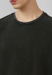 Schwarzes Baumwoll-T-Shirt mit Rundhalsausschnitt, das über eine weiche Textur und subtile Nähedetails am Kragen verfügt.