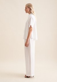 Camicia bianca a maniche corte con colletto, abbinata a pantaloni larghi a gamba dritta. Tessuto morbido e dettagli di design essenziali. Sandali neri.