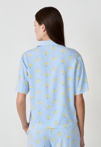 Korte mouwen blauwe shirt met een geel fruitpatroon op een gestreepte achtergrond. Lichtgewicht stof, relaxte pasvorm en klassieke kraagontwerp.