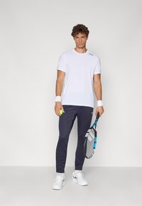 White short-sleeve athletic shirt, navy joggers, white sneakers, tennis racket, and ball. Smooth fabric, fitted silhouette, minimalistic design.