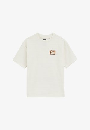 Krém színű, rövid ujjú póló, amelyen egy kis barna hímzett naplogó található egy négyzet alakú folton. Textúrált anyagból készült.