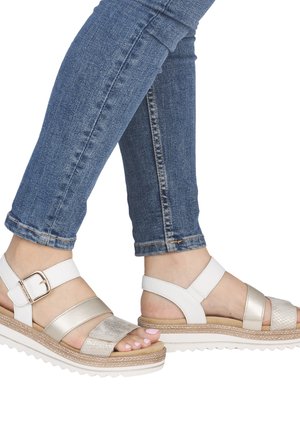 Fødder iført hvide og beige platformssandaler med spærestropper, kombineret med blå oprullede skinny jeans.