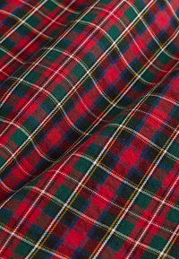 Tissu tartan rouge et vert à motif à carreaux, présentant des lignes blanches et jaunes, mettant en valeur un tissage texturé.