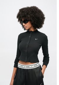 Μαύρο ριμππέν μακρυμάνικο τοπ με ψηλό γιακά και κουμπιά μπροστά, συνδυασμένο με μαύρο σατέν τζόγκερ με λευκή ζώνη μέσης με λογότυπο Nike.