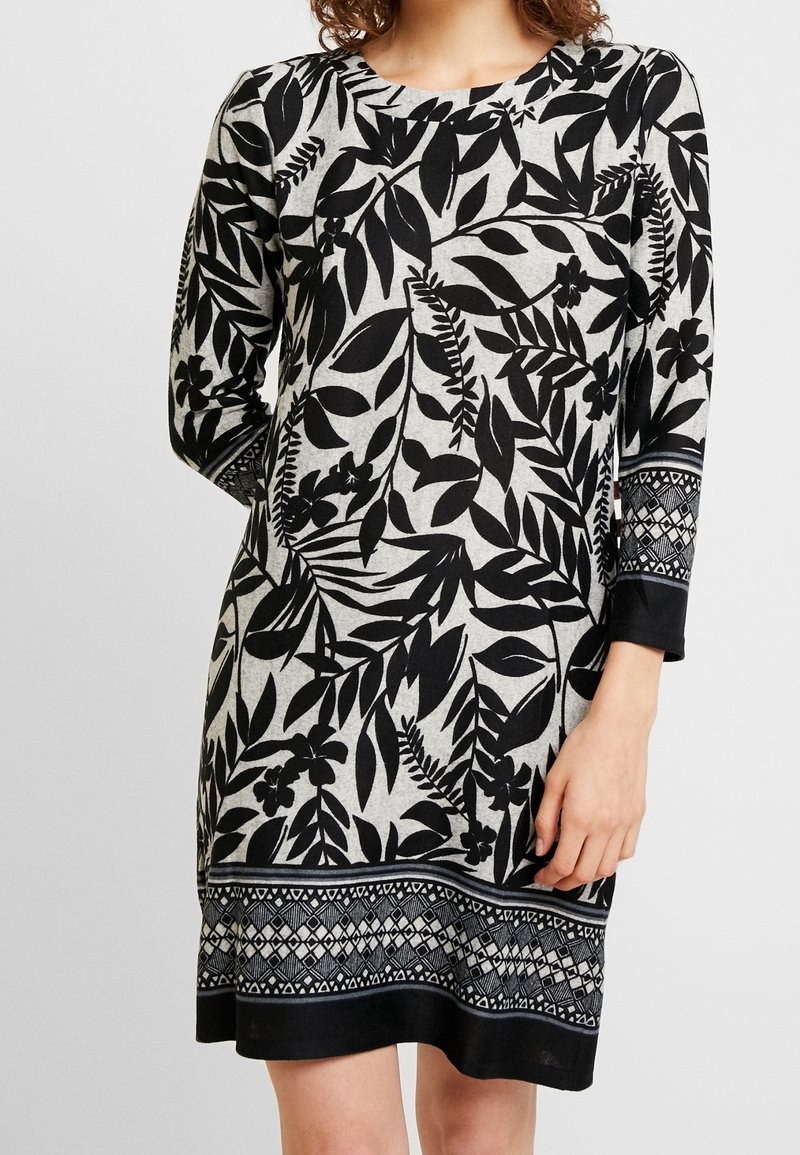 Robe à motifs floraux noirs et gris, manches longues, encolure ronde, avec détail décoratif à l'ourlet présentant des accents géométriques.
