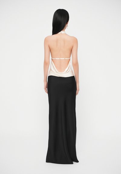 Τοπ ατελείωτο από σατέν σε κρεμ απόχρωση με ραμμένη πλάτη και ρυθμιζόμενο λουράκι· συνδυασμένο με εφαρμοστή μαύρη φούστα μακρύ μήκος, που ρέει μέχρι το πάτωμα.