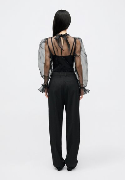 Μαύρη διαφάνεια μπλούζα με πούφ μανίκια και λεπτομέρεια με κορδόνι πίσω, συνδυασμένη με μαύρο παντελόνι ψηλόμεσο, που διαθέτει ομαλή, ρέουσα υφή.