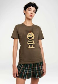 Braunes Baumwoll-T-Shirt mit einer Cartoon-Biene mit gestreiftem Körper und Gesicht, kombiniert mit einem grünen karierten Faltenrock.