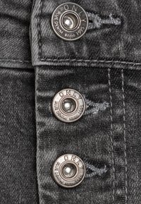Vaqueros de denim gris oscuro con tres botones plateados visibles que presentan el logotipo emblema de la marca "ONLY" y costuras en contraste. Tejido texturizado.