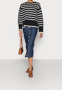 Svart och vit randig stickad tröja, knapplistad denimkjol, bruna loafers och en brun handväska. Outfiten är avslappnad och lager-på-lager.