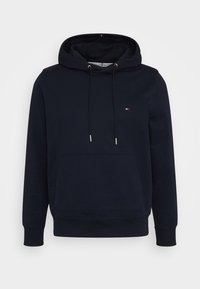 Sweat à capuche bleu marine avec poche kangourou à l’avant, capuche avec cordon, poignets et ourlet côtelés, et petit logo rouge, blanc et bleu sur la poitrine.